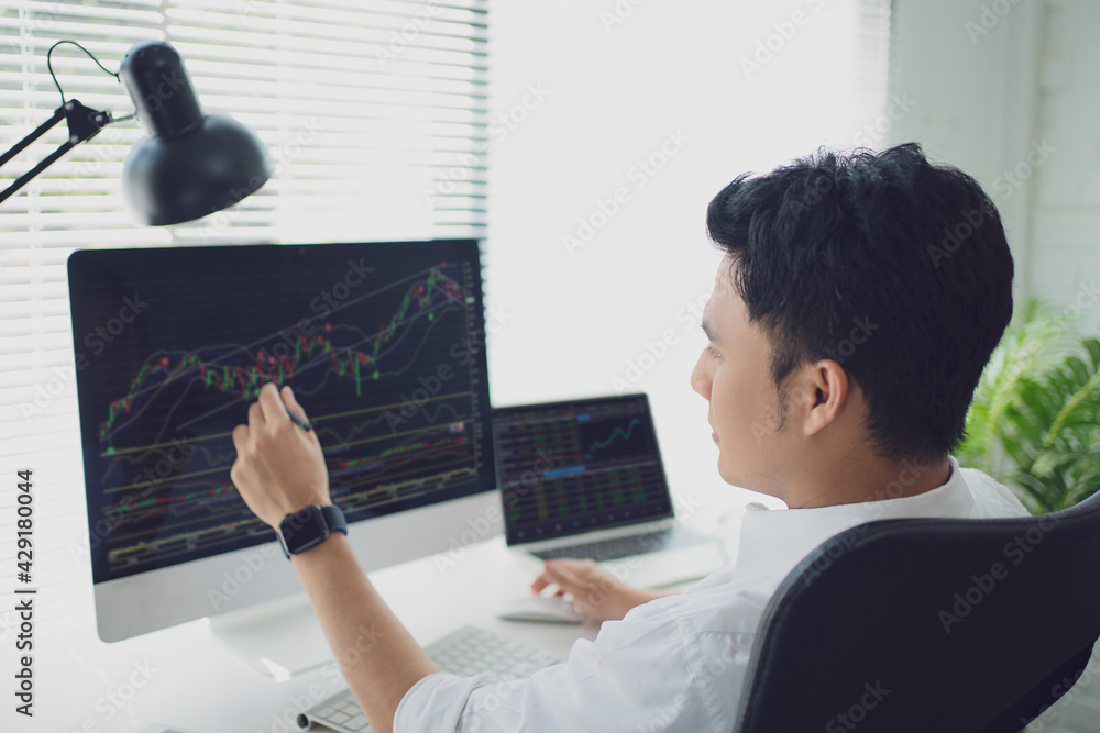 Poster young businessman pointing graph data on a computer screen with a pen while working in a modern offi