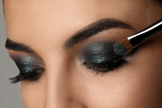 Applying dark eye shadow with brush onto woman's face, closeup. Beautiful evening makeup