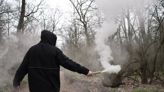 A man with a smoke grenade from which smoke comes from the forest. The man signals the sauce because he got lost in the woods. A man during a protest with a smoke grenade.