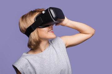 Side view photo of a caucasian woman with blonde hair smiling wearing virtual reality headset on a purple background