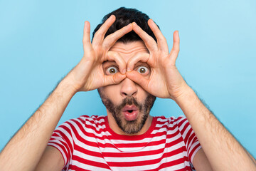 Photo of funny shocked young guy wear red showing spectacles fingers cover eyes isolated blue color...