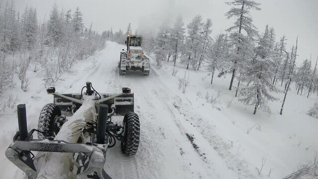 Two graders ride on the snow-covered cold tundra
