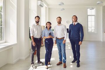 Fototapeta premium smiling business partners or project team standing and looking at camera in modern office