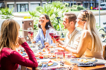 Multiracial people drinking red wine at open bar restaurant - Group of friends laughing having fun dining together outdoor -  Bright filter