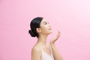 Asian girl with perfect glowing skin and nude natural makeup posing against pink background.