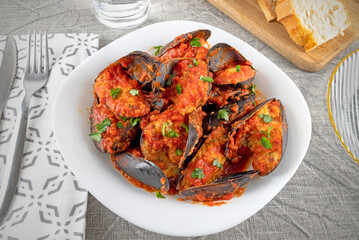Stuffed mussels with tomato sauce and parsley on the white plate.