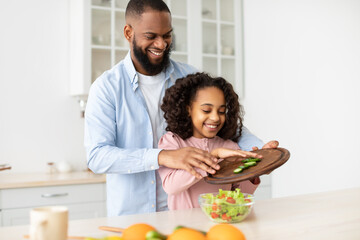 Cheerful afro father and daughter cooking salad together