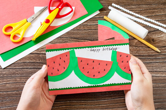 The child is holding summer birthday card with watermelons with birthday greetings. Handmade. Childrens creativity project, crafts for kids.