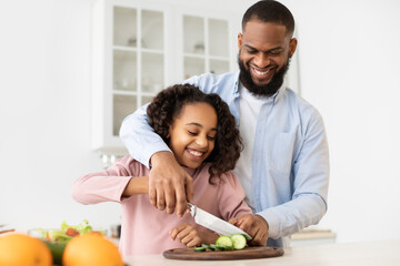 Afro father teaching daughter how to prepare salad