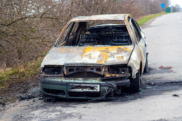 Obraz na płótnie Canvas Burned car after an accident on the asphalt road. Front view. Arson of a car, criminal showdowns