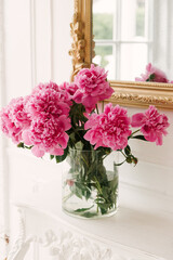 A bouquet of fresh pink peonies in a transparent vase in a luxurious interior