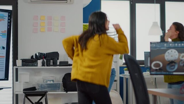 Multiethnic happy women dancing cheerfully in startup business office, during work hours, celebrating victory of construction project. Afterparty in workplace, colleagues having fun in free time
