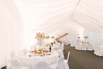Luxury wedding dinner in a large beautiful tent, beautiful decor for the wedding of the white hall decorated with flowers