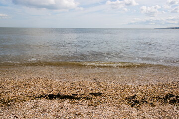 Beach and sea landscape on a sunny spring day, view over Thames estuary, during high tide, Isle of Grain, UK, Kent, England