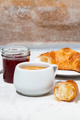 cup of espresso and fresh croissants, berry jam for breakfast on white table, closeup