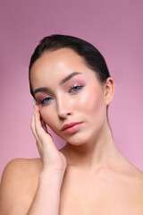 Portrait of young beautiful woman with perfectly clean face skin wearing professional make up touching her face. Female with long black hair tied in a ponytail. Close up, copy space, background.