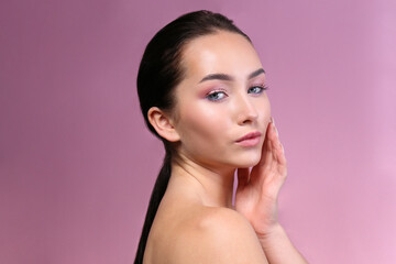 Portrait of young beautiful woman with perfectly clean face skin wearing professional make up touching her face. Female with long black hair tied in a ponytail. Close up, copy space, background.