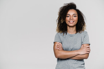 A smiling curly-haired woman standing with crossing arms in front of her while standing in the...