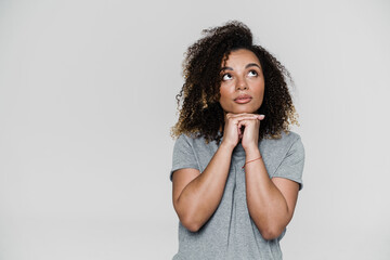 A pensive woman looking-up with hands propping her chin while standing in the studio