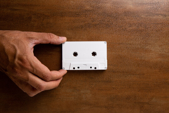 A man's hand grabs a white magnetic audio tape on a wooden base. Audio cassette. Music.