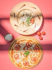 Italian fettuccine pasta and traditional pizza margherita with tomato on pink abstract background.