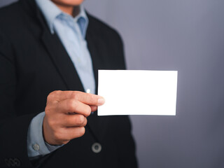 Businessman showing a blank white business card while standing with a gray background. Close-up photo. Space for text. Business and contact concept