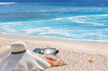 Fototapeta na wymiar Chapeau de paille, lunettes de soleil et coquillages sur plage paradisiaque 