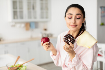 Smiling doubtful woman holding red apple and donut