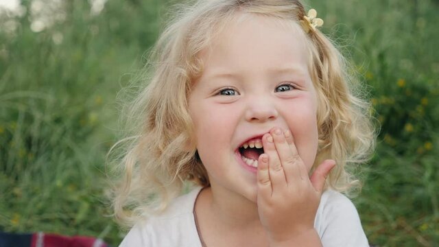 Little blonde girl laughing funny covering her mouth with her hand