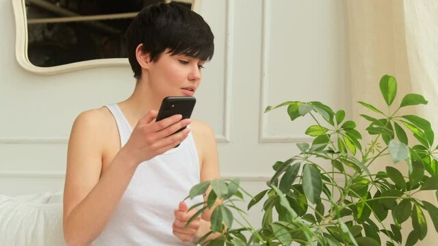 Young woman takes pictures photographing of a house plant uses a smart phone. Shares indoor plant leaves care in the mobile application.