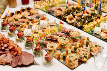 Beautifully decorated catering banquet table with burgers, profiteroles, salads and cold snacks. Variety of tasty delicious snacks on the table