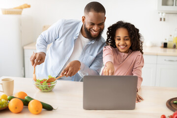 Black man and girl cooking in kitchen reading online recipe