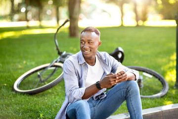 Fototapeta premium Cool black guy with modern bike using smartphone at park
