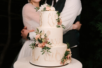 Luxury wedding tiered white cake decorated with flowers, photo at night on the background of the...