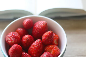 Bowl of fresh strawberries and open book on a table. Selective focus.