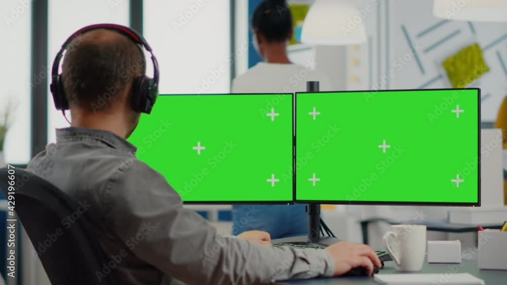 Poster employee with headphones using dual monitror setup with green screen, chroma key mock up isolated di