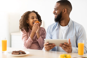 Fototapeta na wymiar Black father and daughter eating sweets using tablet
