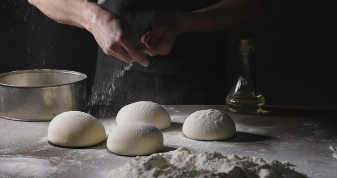 Chef prepares dough for traditional Italian pizza. Cooker sprinkles flour on dough in kitchen, 4k footage