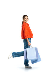 full length of young positive woman in orange shirt holding shopping bags isolated on white
