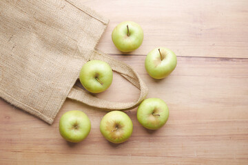 top view of green apple and reusable shopping bag on wooden background 