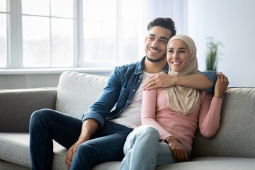 Positive arab couple sitting on couch at home