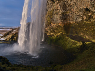 Fototapeta na wymiar Stunning view of the bottom of famous waterfall Seljalandsfoss in the south of Iceland with moss-covered colorful rock face in the beautiful evening light in winter season.