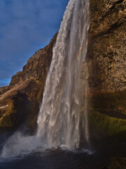 Beautiful side view of famous waterfall Seljalandsfoss on the southern coast of Iceland near ring road with colorful rainbow in between in the evening sun in winter season.