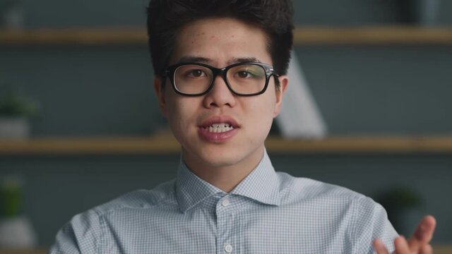 Online blog. Camera pov of young asian guy in eyeglasses talking to camera, discourcing about global news