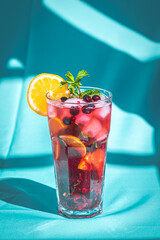 Ice refreshing summer drink with berry and lemon on abstract blue background.