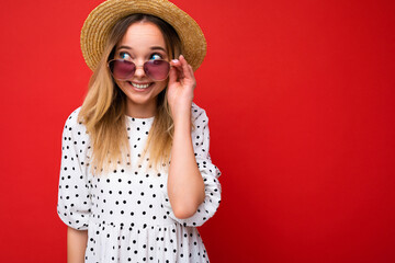 Photo shot of beautiful positive smiling happy joyful young blonde woman wearing summer casual clothes and stylish sunglasses isolated over colorful background looking to the side