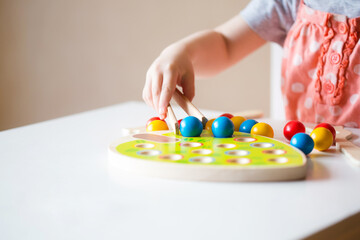 small baby lays out balls with tweezers in holes . concept of fine motor skills development, teaching preschool children
