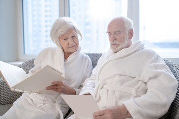Mature couple in white robes choosing procedures in a spa center