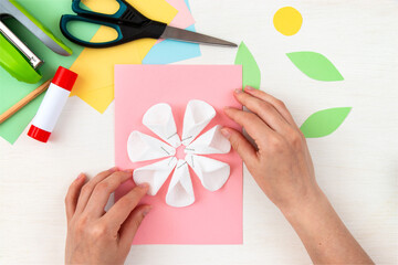 A flower made of cotton pads. Colored paper, stapler, scissors, scissors, pencil on a white table. Children's craft card for mother's day. Step-by-step instruction. Step 7.