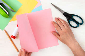 Empty pink paper with place for text. Colored paper, stapler, scissors, scissors, pencil on a white table. Children's craft card for mother's day. Step-by-step instruction. Step 11.